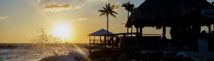 A beautiful sunset on a beach in Curacao with a beach front bar and waves crashing into the shore