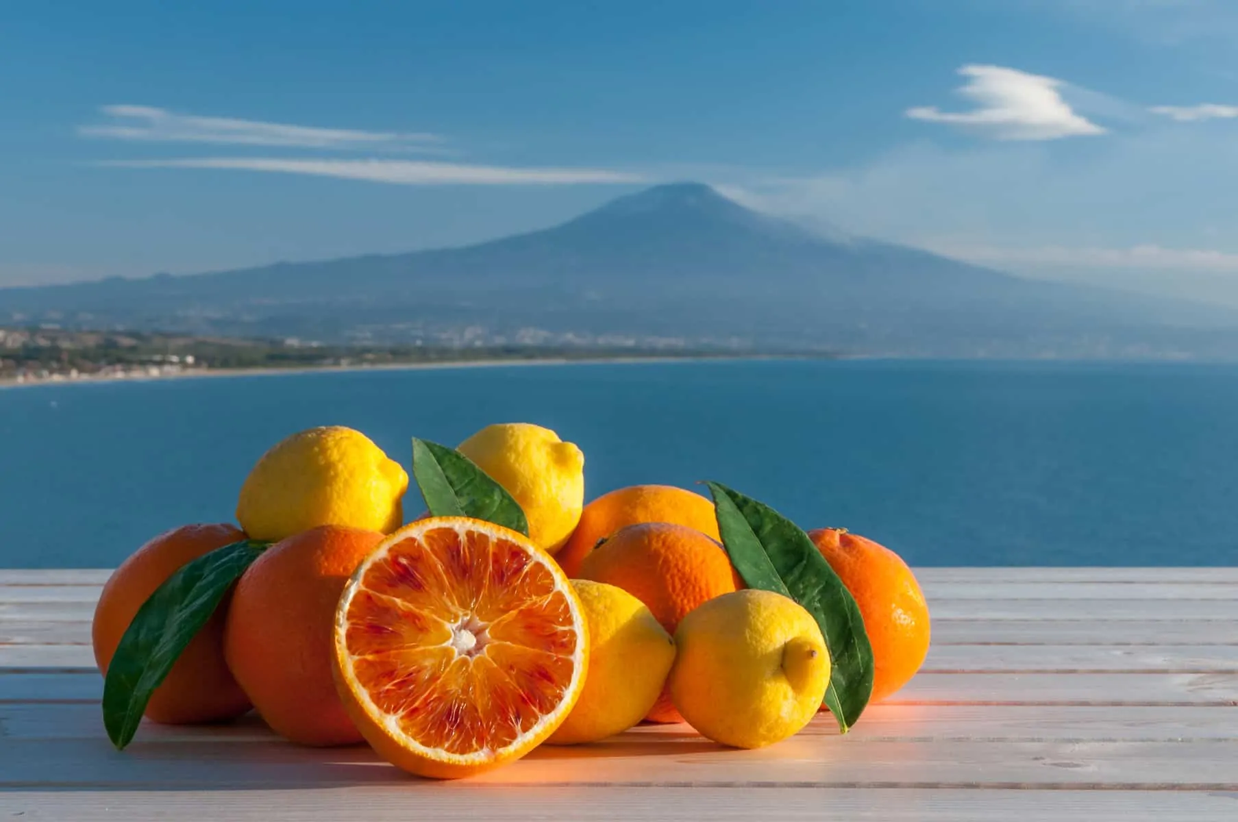Oranges and lemons on a wooden table with blue sea, Mount Etna and clouds in the background
