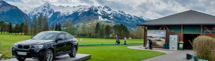 Golfferie i Tyskland. ZELL AM SEE, Luxury BMW X6 på pedestal i Golfclub Kaprun Zell am See. Black BMW on green of golf course with Alps in background