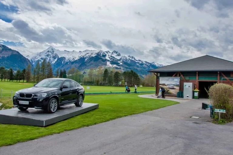 Golfrejser i Tyskland. ZELL AM SEE, Luxury BMW X6 på pedestal i Golfclub Kaprun Zell am See. Black BMW on green of golf course with Alps in background
