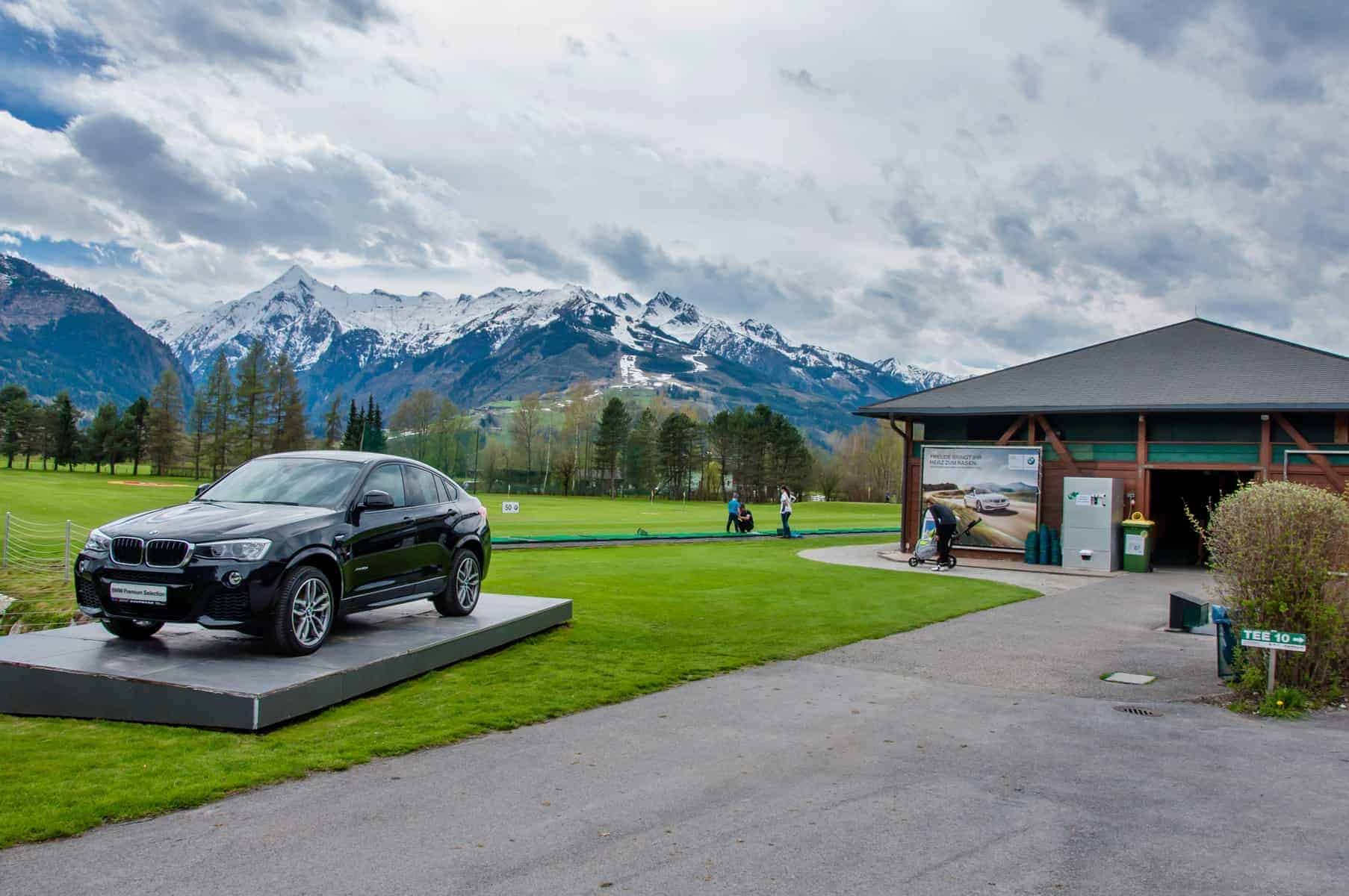 Golfferie i Tyskland. ZELL AM SEE, Luxury BMW X6 på pedestal i Golfclub Kaprun Zell am See. Black BMW on green of golf course with Alps in background