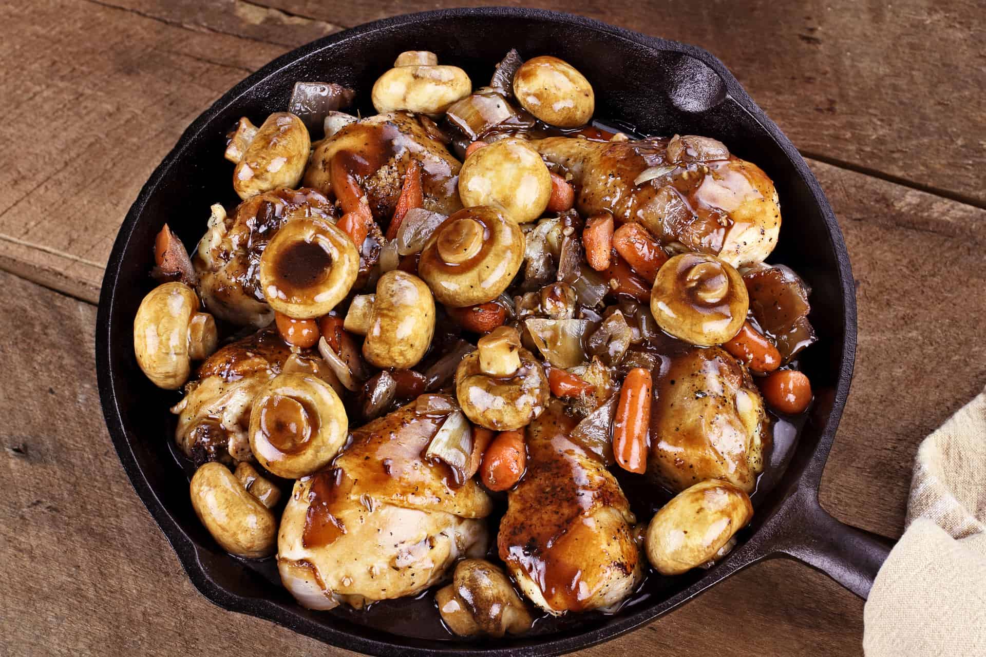 Coq Au Vin in rustic cast iron pan with shallow depth of field.
