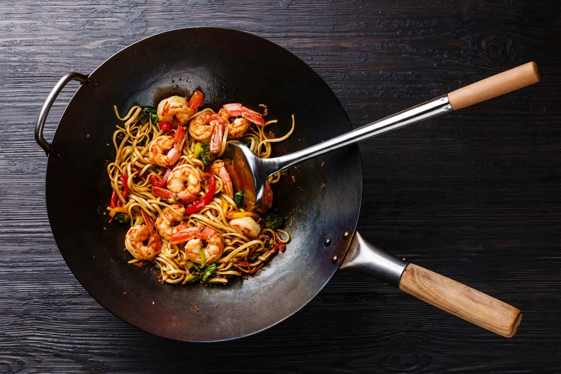 Udon stir-fry noodles with shrimp and vegetables in wok pan on black burned wooden background