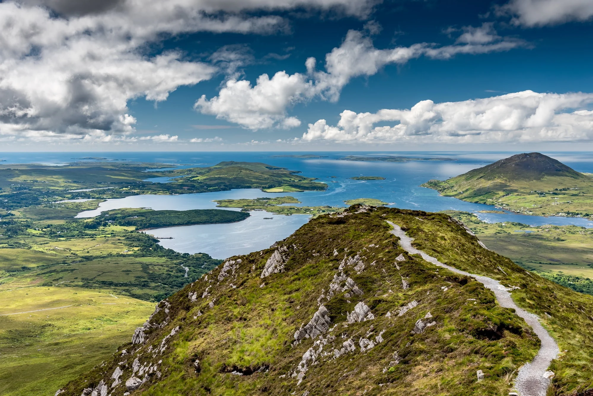 The hiking trail at the top of Diamond Hill in Connemara National Park, Ireland. Behind, the sun plays with the clouds reflected in the sea.