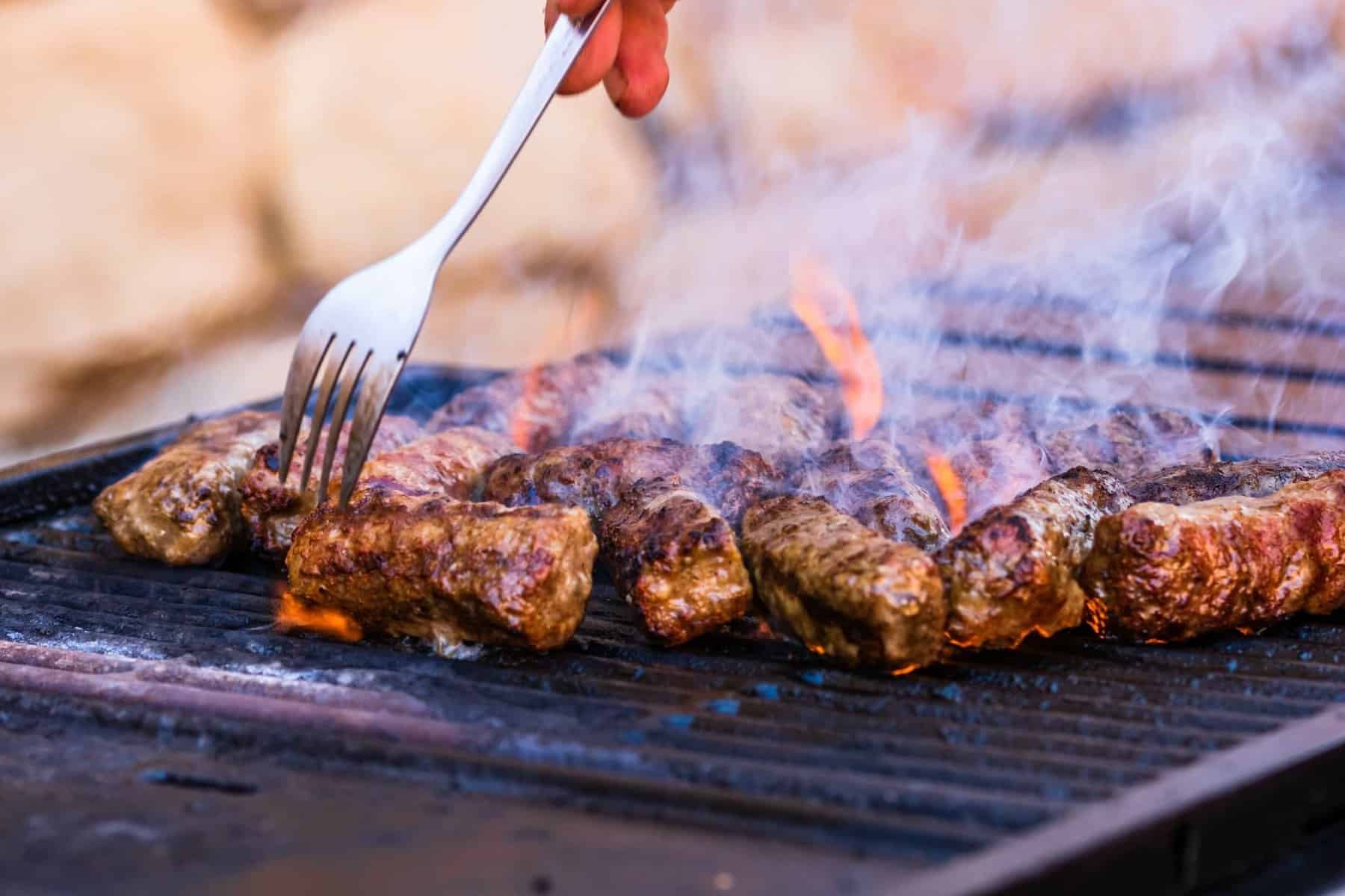 Closeup of hand preparing meat rolls called mici or mititei on barbecue with rising smoke