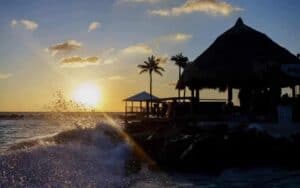 A beautiful sunset on a beach in Curacao with a beach front bar and waves crashing into the shore