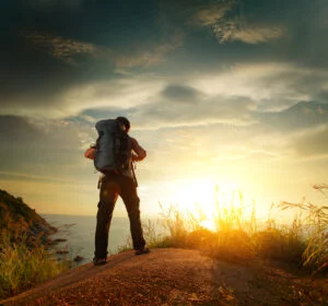 Book dinrejse fx Adventure rejser i hele verden (Hiker with backpack standing on a rock and enjoying sunset over sea) Bookdinrejse her
