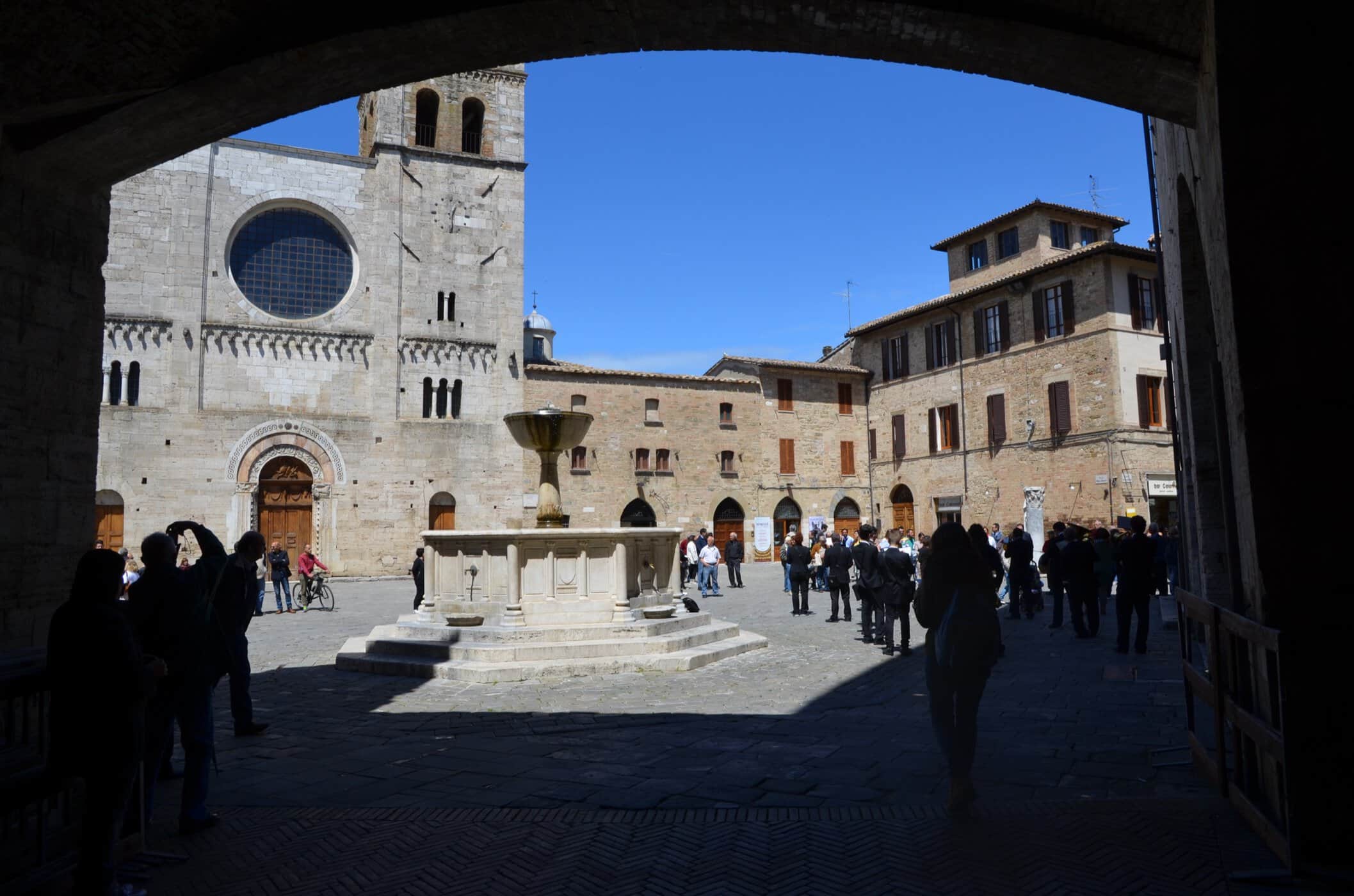 Piazza Silvestri i Bevagna set gennem en portbue med den romanske kirke San Michele og springvandet